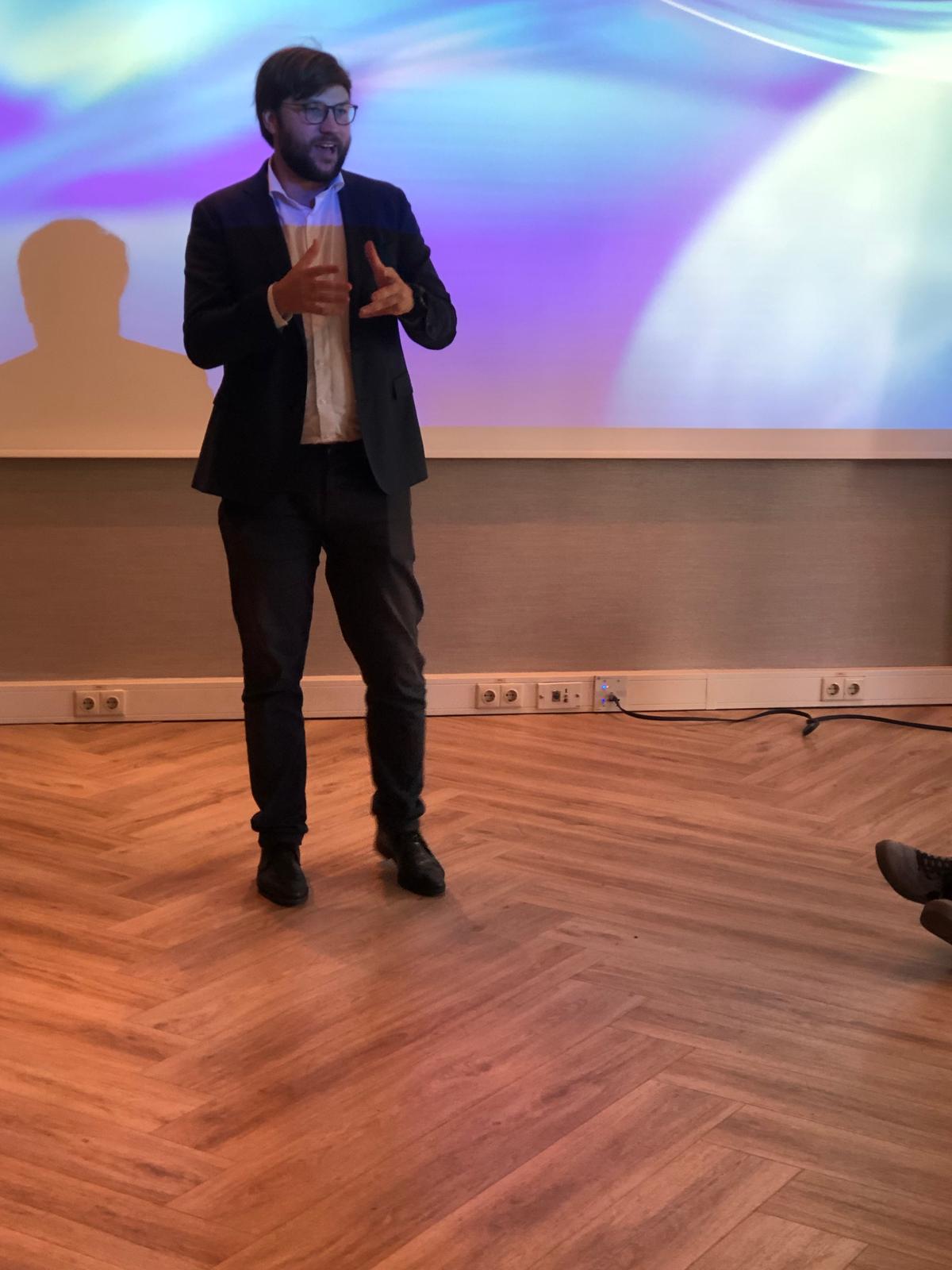 Damian presenting to a group, standing in front of a projection screen