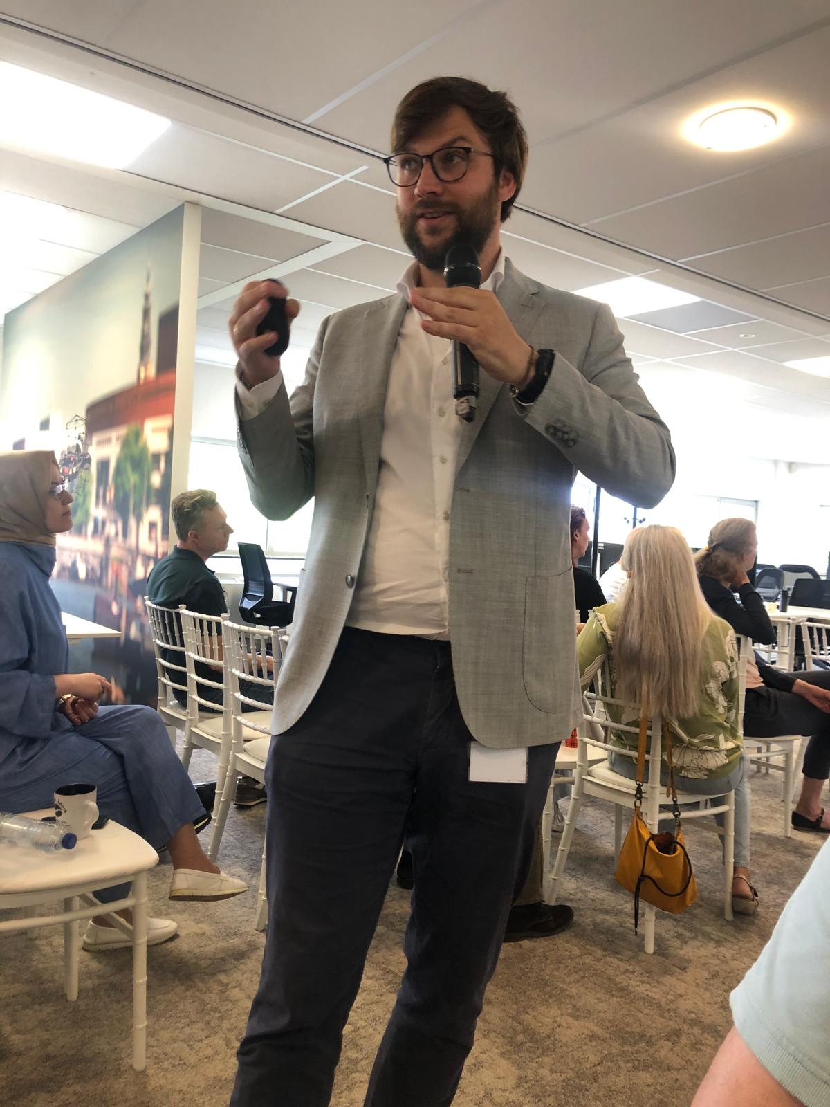 Damian speaking with a microphone during a session, participants seated around him